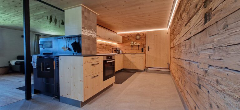Vollholzküche in Fichte rustikal mit schwarzer Arbeitplatte aus Keramik und Holzofen