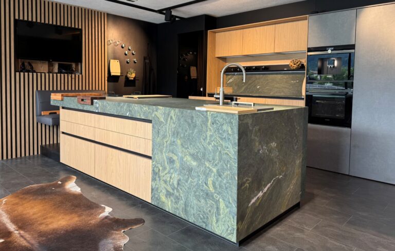 moderne olina Küche mit Strasser Naturstein in grün, Fronten in grau matt kombiniert mit Naturholz in Eiche und direkter Sitzmöglichkeit mit Arbeitsplatte als Theke