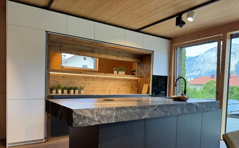 Küchen mit weißen Hochschränken in matt sowie einer Insel mit Arbeitsplatte in Naturstein mit Bruchkante, schwarzer Quooker Armatur