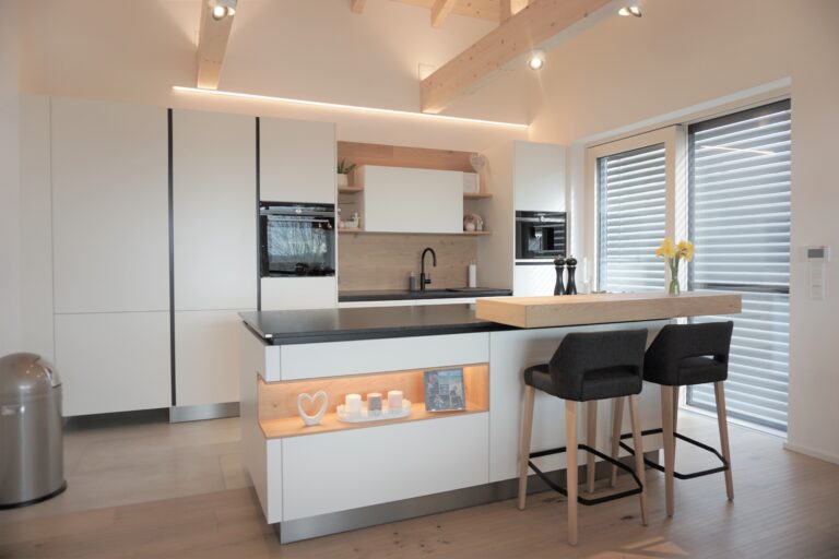 Küche in weiß mit Insel mit schwarzem Naturstein, Theke mit zwei Stühlen