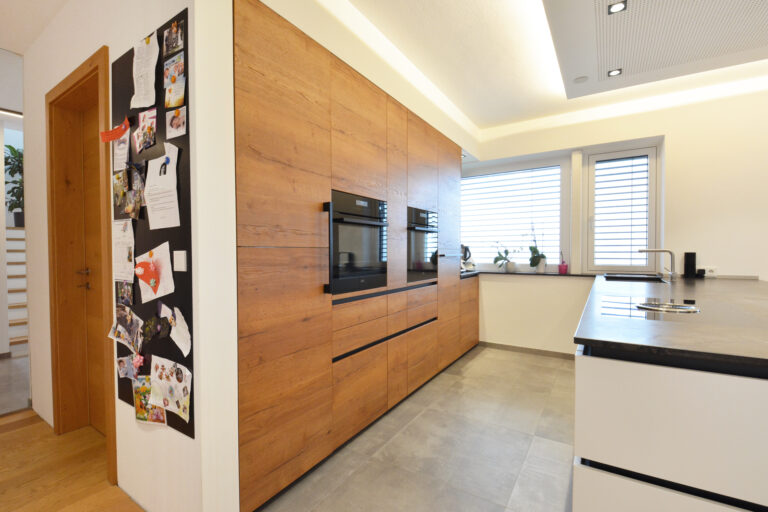 Küche mit Insellösung, Hochschränke in Wildeiche natur , Arbeitsplatte aus schwarzem Naturstein