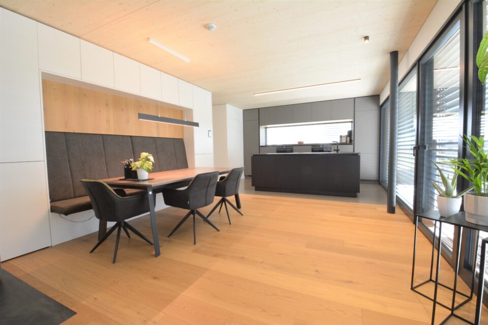 Küche mit grauer Front - Insel mit Fronten in schwarz matt, Sitgruppe mit tisch in Eiche, Sitzbank und drei Stühlen