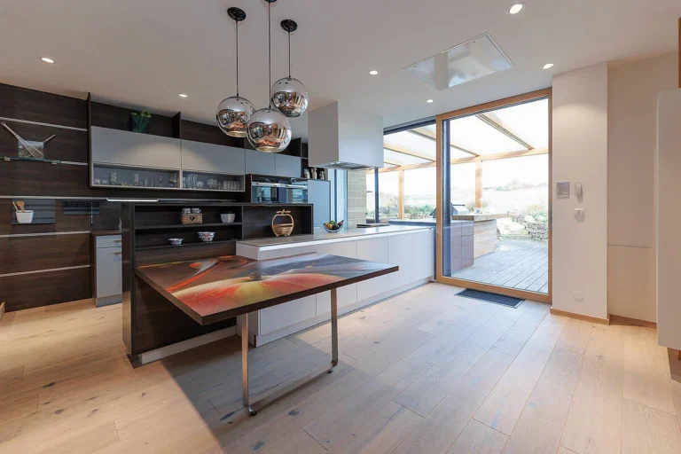 olina I-Küche in dunkelm Holz und hellgrauen Fronten mit weißer Insel und angebauten Esstisch kombiniert