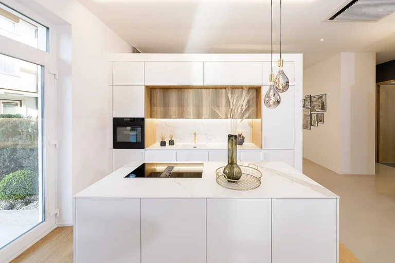 Weiße Küche mit Hochschränken in Naturholzlamellen, weiße Insel mit weißer Keramikarbeitsplatte in Marmoroptik